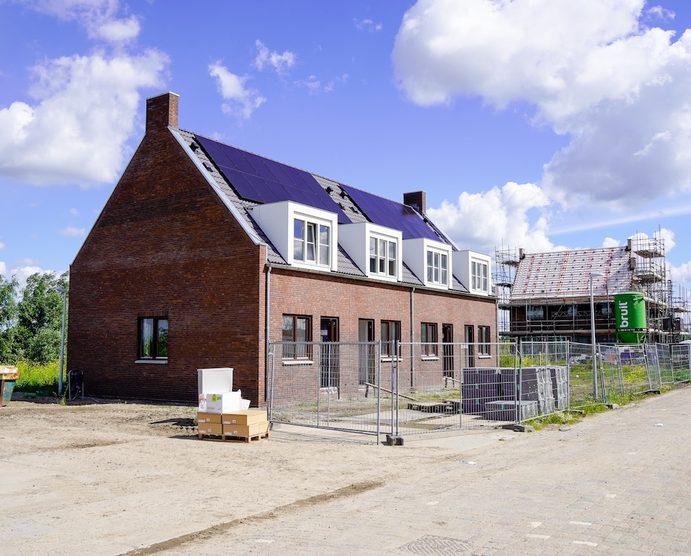 Nieuwbouwwoningen in aanbouw in de wijk 't Suyt, met zonnepanelen op het dak en bouwmaterialen op de voorgrond onder een blauwe lucht met wolken.